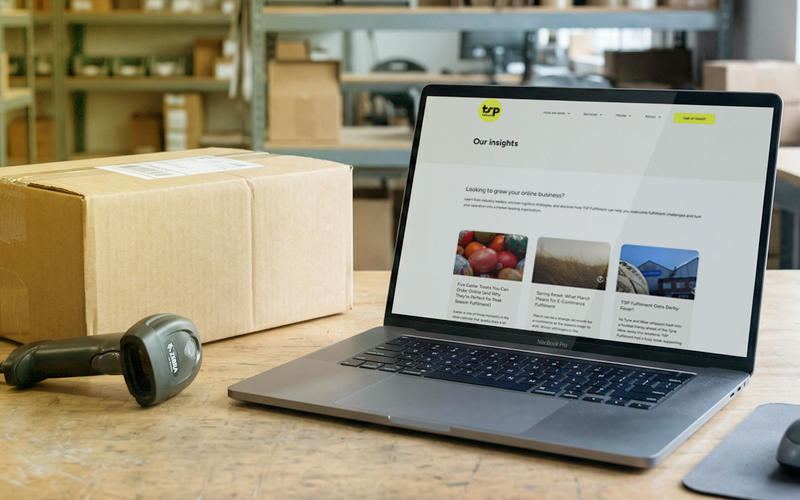 The image shows a workspace with a laptop, barcode scanner, and packages